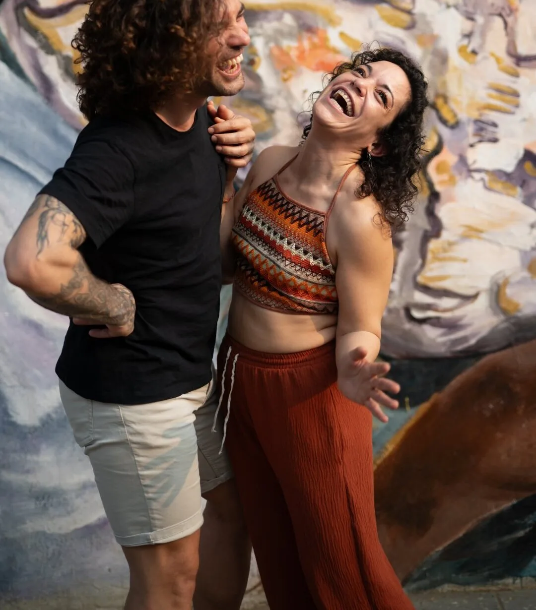 Esther and Ángel laughing in front of a painted mural on a Kerala street.