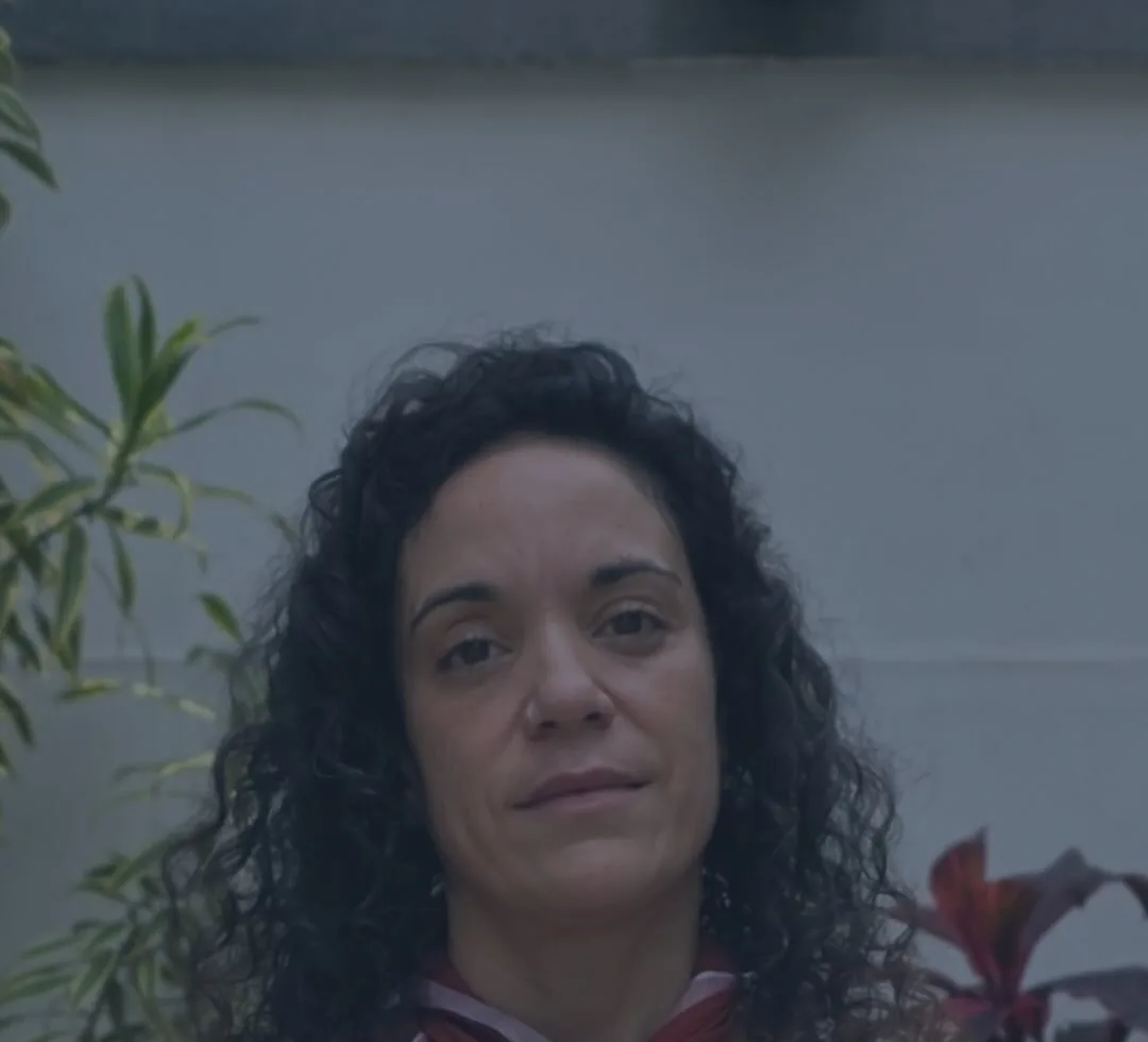 Portrait of Esther Gómez looking at the camera, beside a plant.