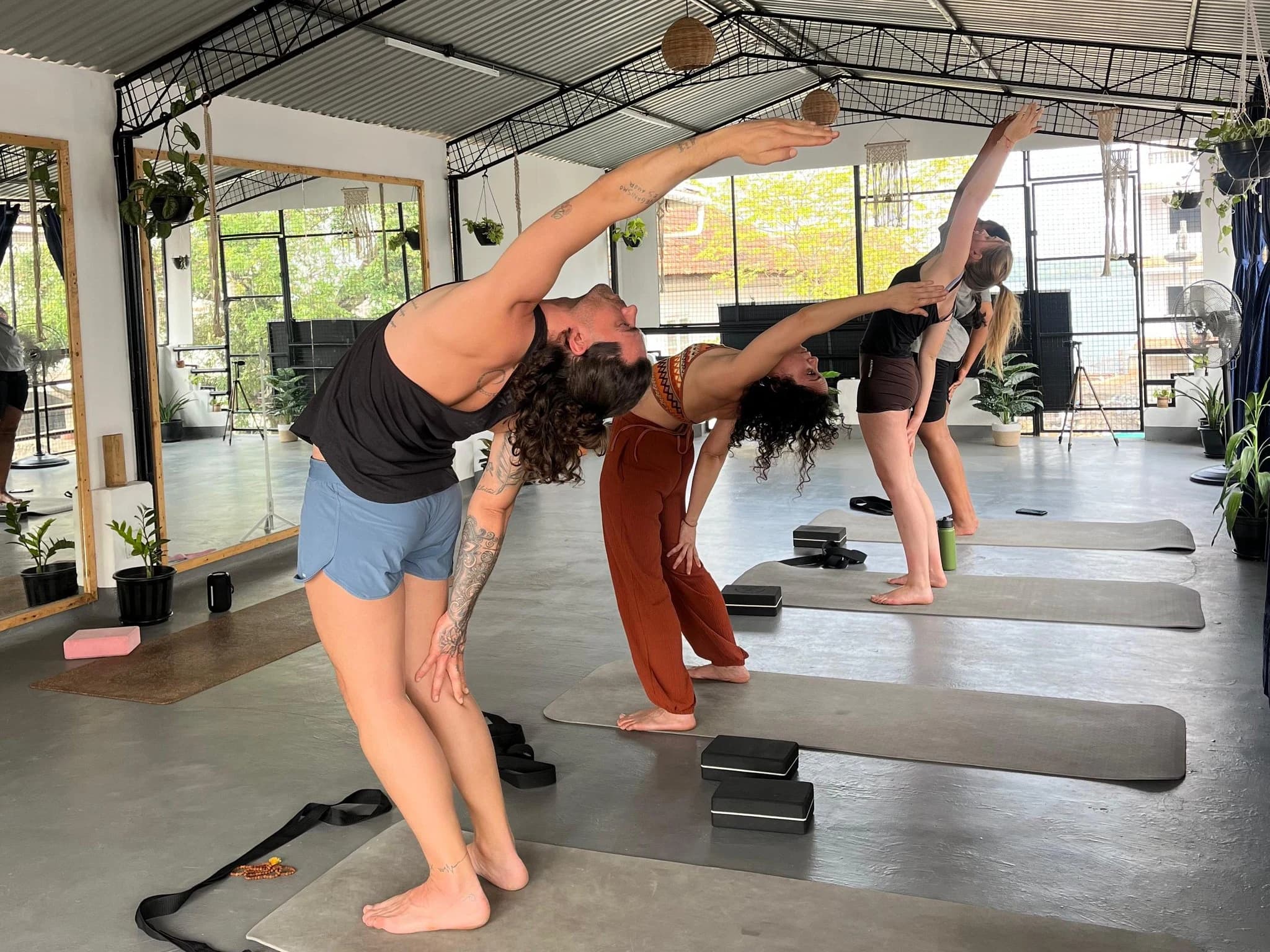A group practising yoga in an open room, morning light coming through the windows.