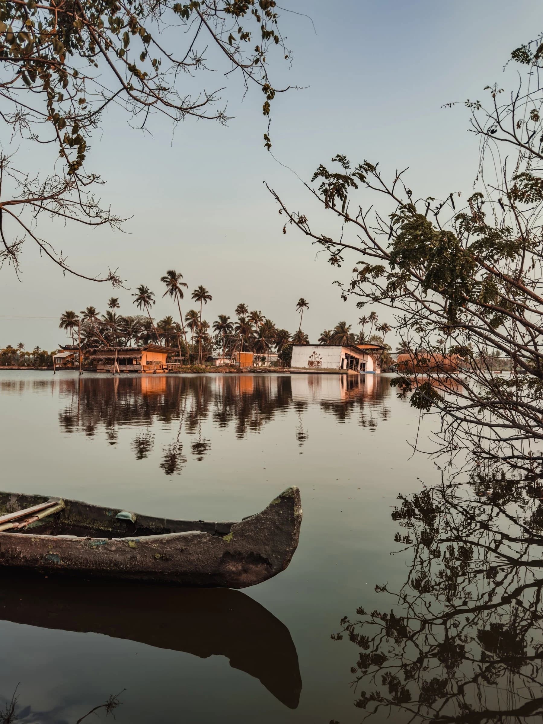 A traditional wooden canoe rests at dawn on the Kerala backwaters, palms and houses reflected in the still water.