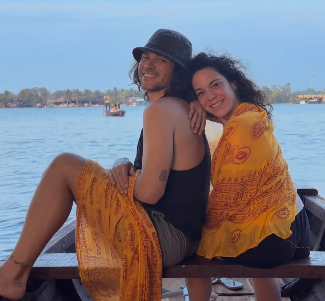 Esther y Ángel sentados juntos en una barca sobre el agua, bajo un cielo azul despejado.