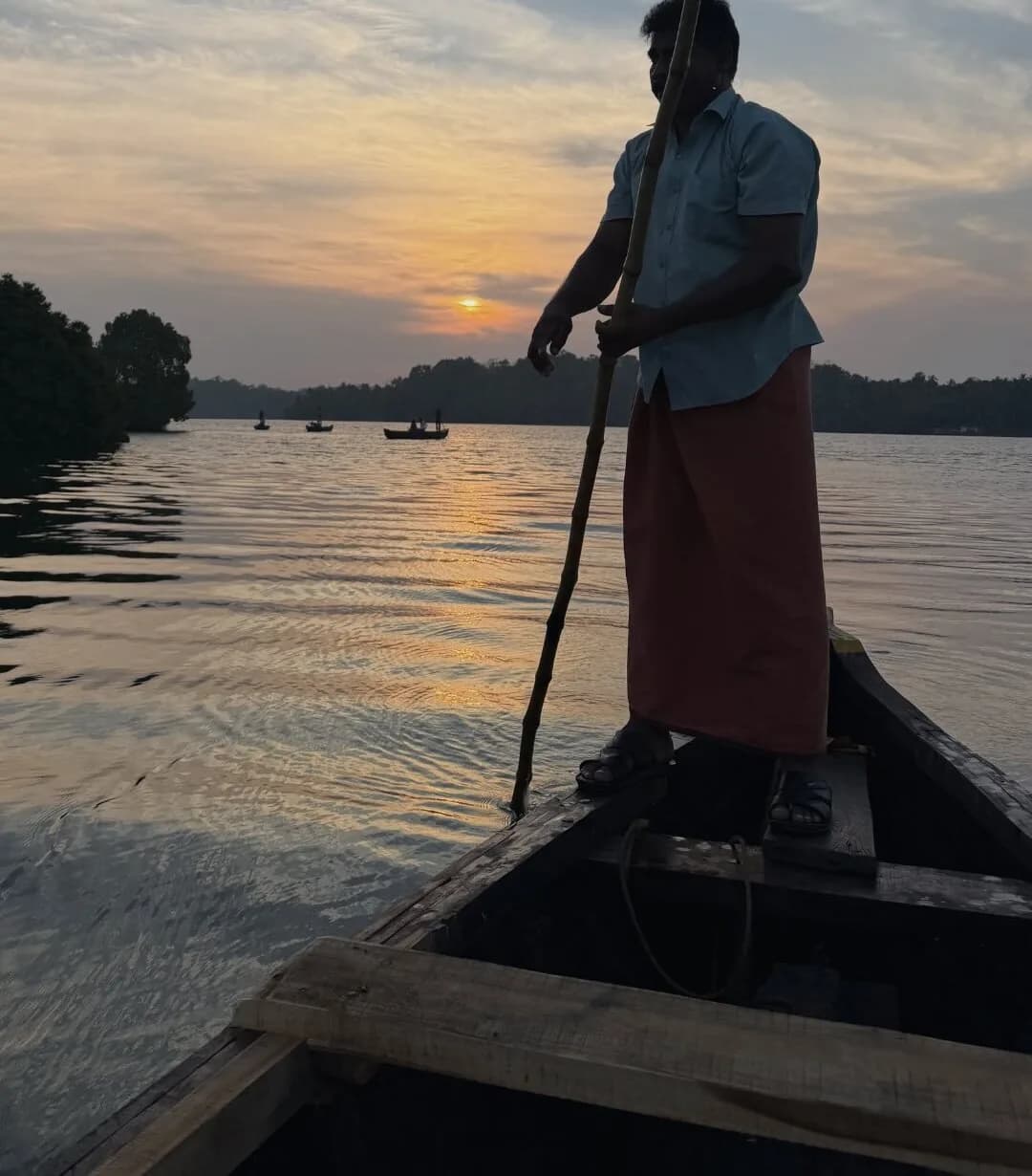 A boatman poles his canoe standing up as the sun goes down over the Kerala canals.