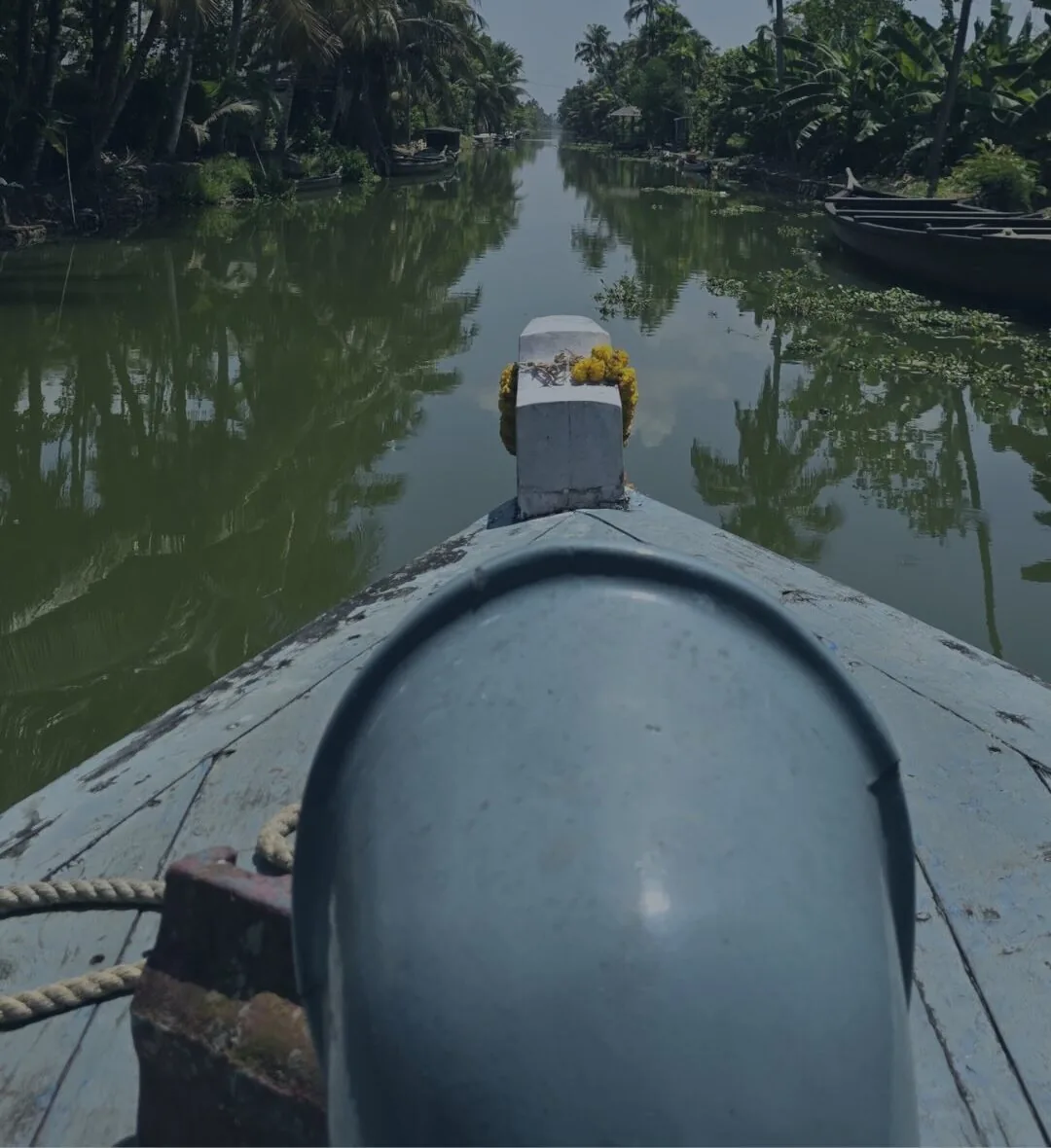 The bow of a boat moving up a narrow canal walled in by dense greenery.
